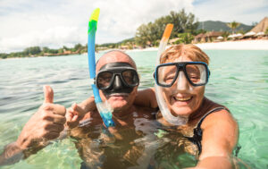 Senior happy couple taking selfie in tropical sea excursion with water camera - Boat trip snorkeling in exotic scenarios - Active retired elderly and fun concept around the world - Warm bright filter